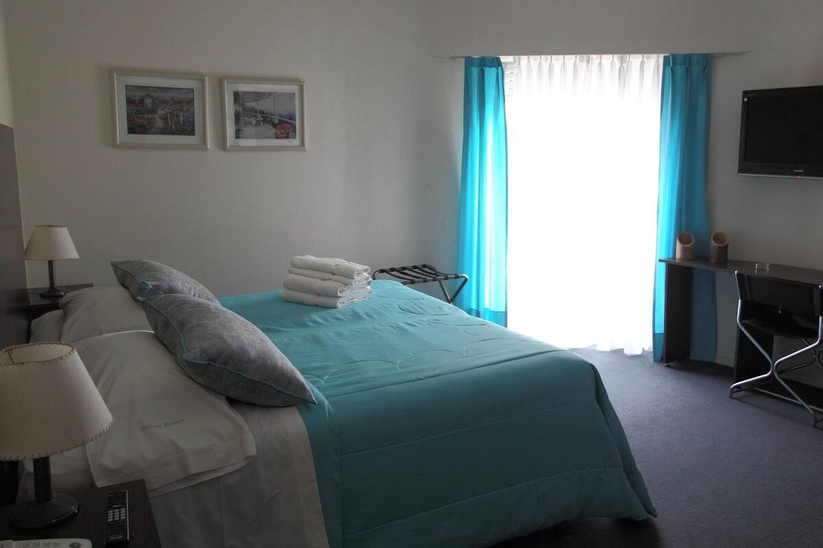 A hotel room with a bed, a desk, a TV, and two framed pictures on the wall.