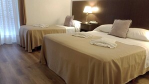 A hotel room with two beds, each with a beige bedspread, a nightstand with a lamp, and a telephone.