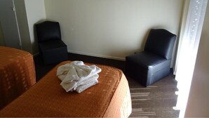 A hotel room with two beds, a flat-screen TV mounted on the wall, and a window with curtains.