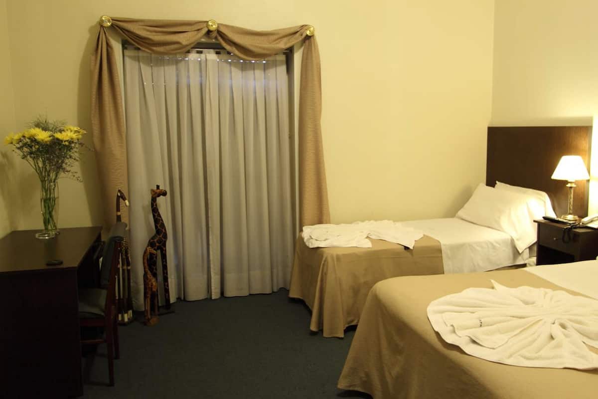 A hotel room with two beds, a desk, a chair, a lamp, and a vase with flowers.