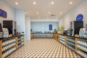 Una cafetería con piso a cuadros, estantes con tazas y vasos, y un letrero que dice 'traer el tocino a casa'.