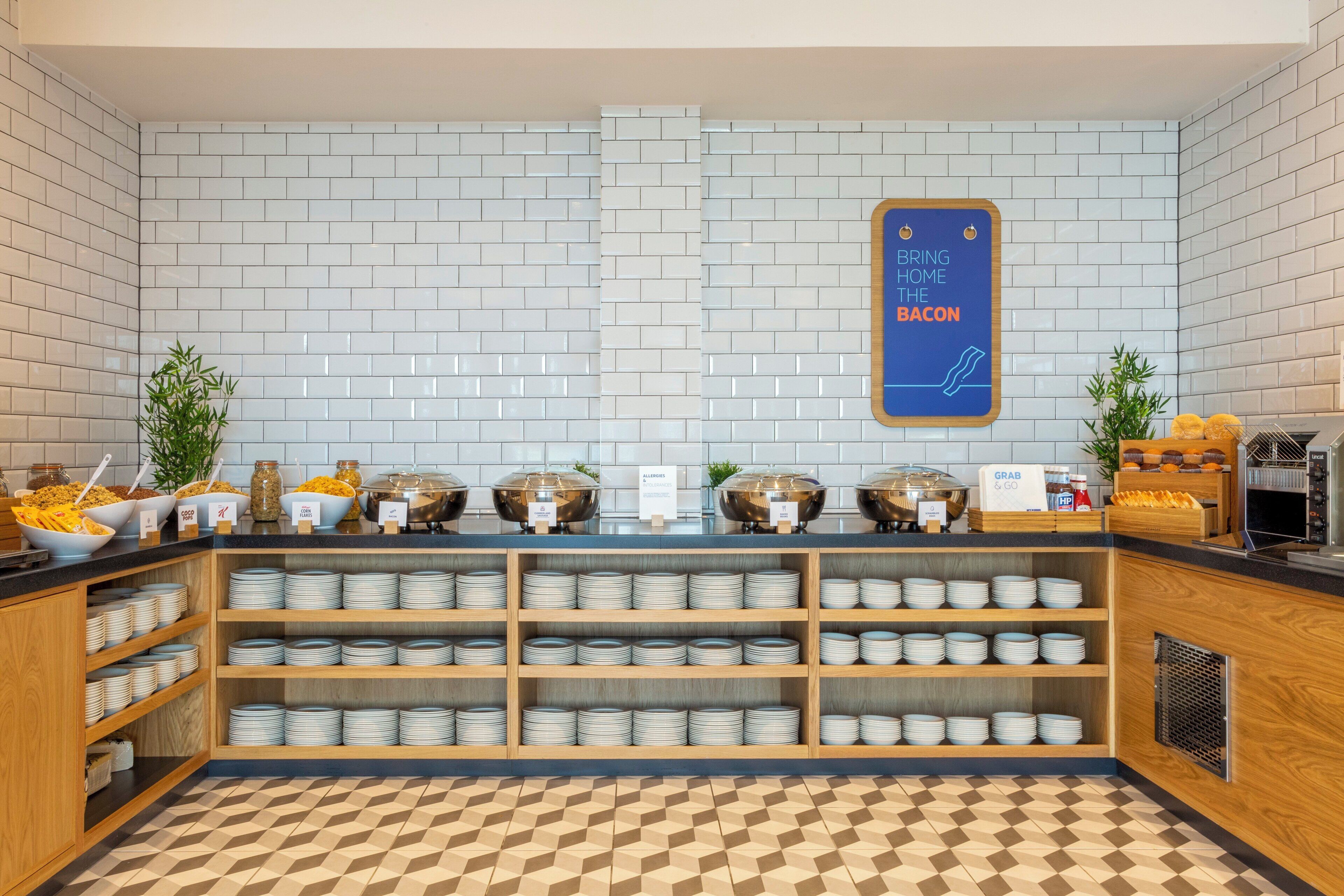 Zona de bufé con diversas opciones de comida, incluyendo cereales, frutas y un cartel que indica la disponibilidad de tocino.