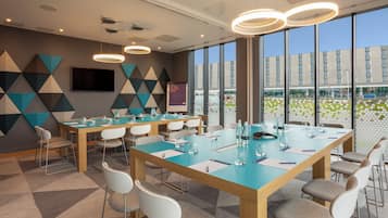 A modern conference room with a large table, chairs, and a large window with a view of a building and greenery.