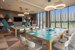 Un moderno salón de conferencias con una gran mesa, sillas y un amplio ventanal con vistas a un edificio y áreas verdes.