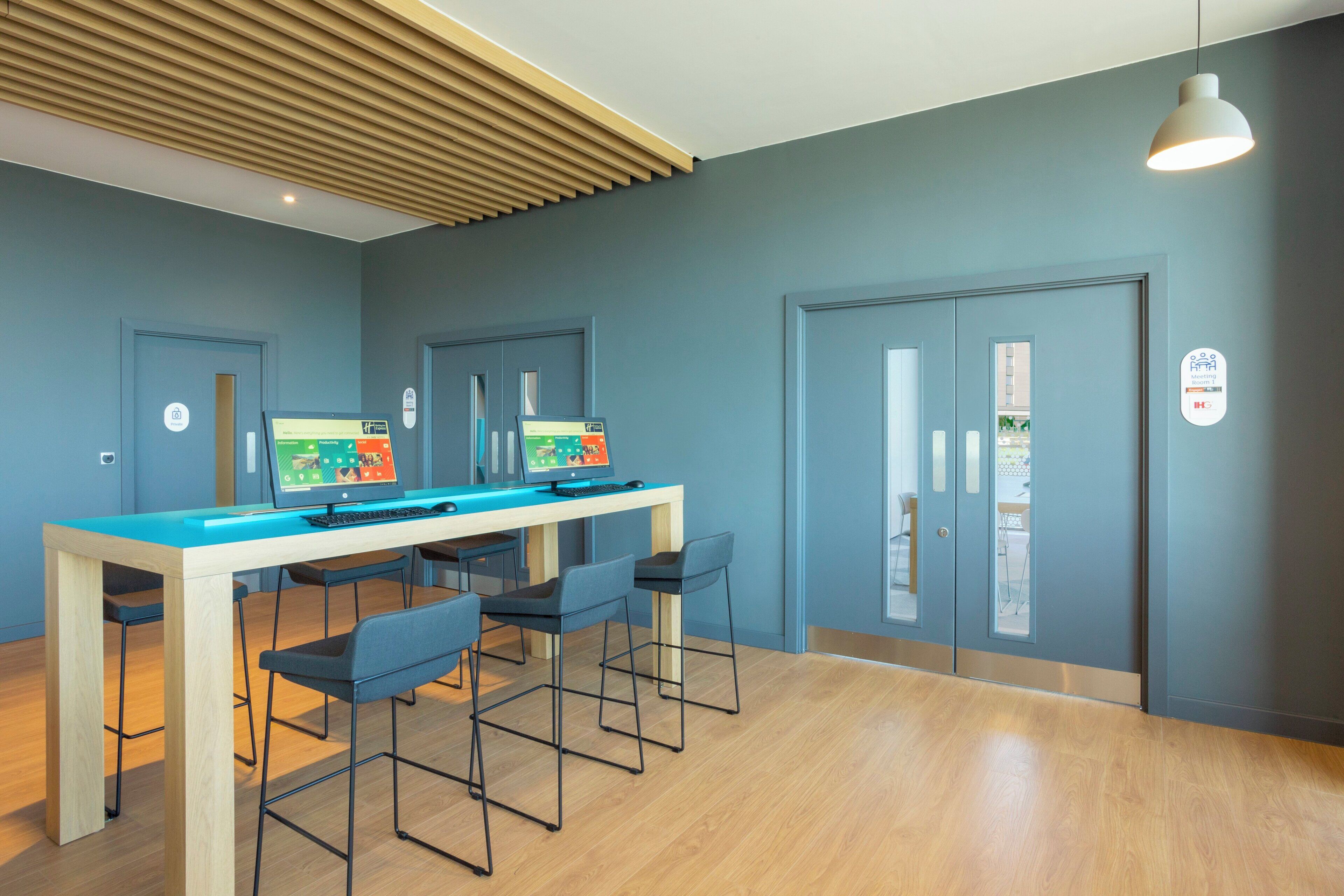 A modern office space with a long table, four chairs, and two computer monitors.