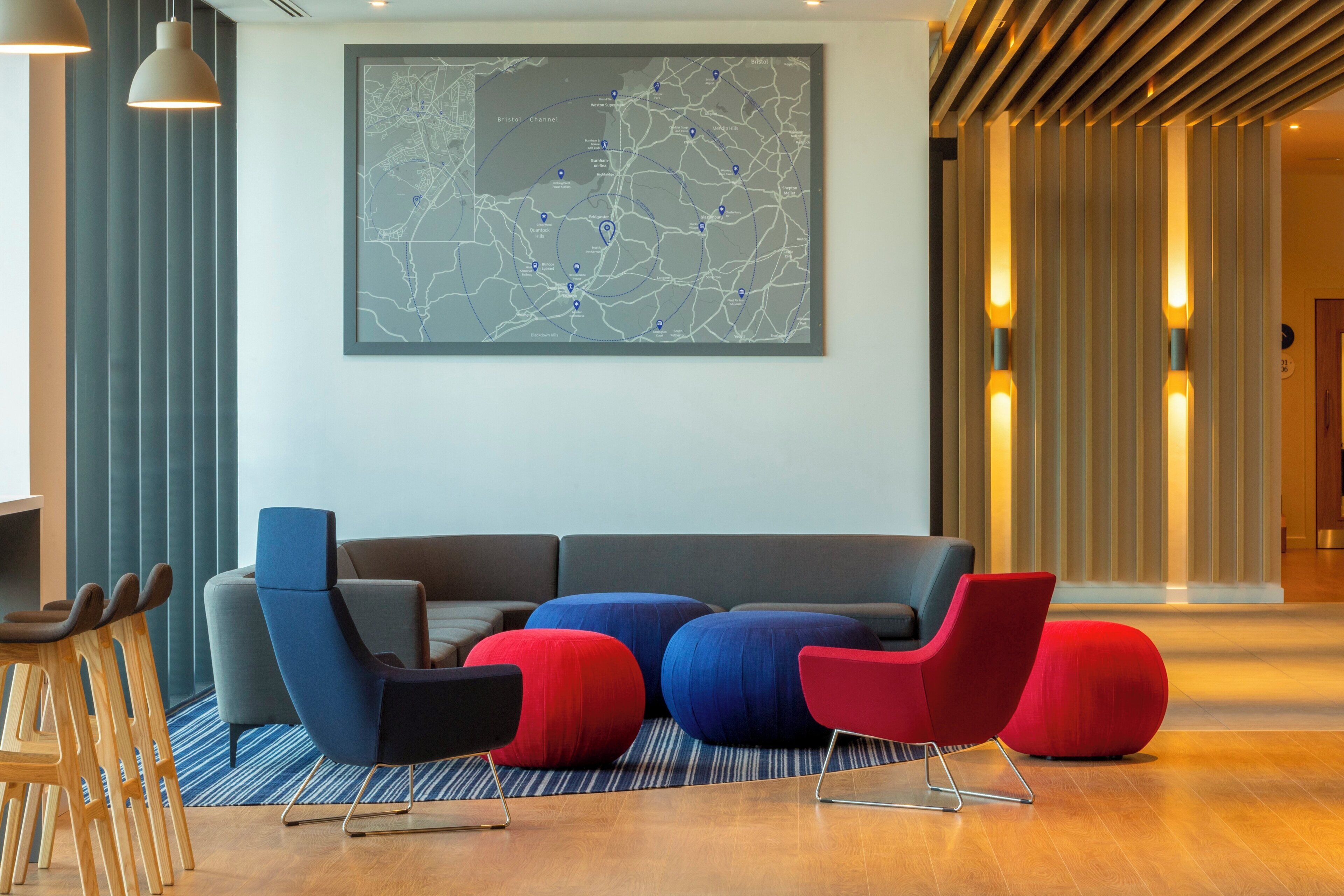 A modern lobby with a large map on the wall, a grey sofa, and red and blue chairs.