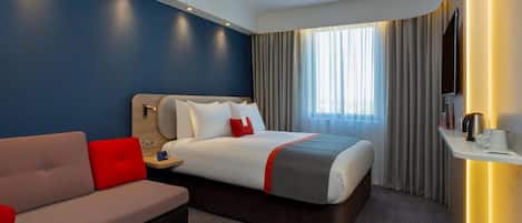 Quarto de hotel com cama, sofá, televisão e janela com cortinas.