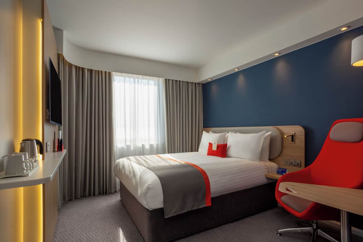 Ein Hotelzimmer mit Bett, Schreibtisch, Stuhl, Fernseher und einem fensterbepflanzten Fenster.