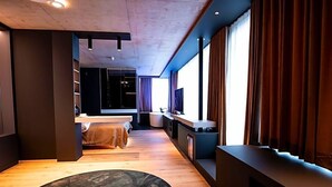 A modern hotel room with a wooden floor, a round rug, a bed, a TV, and a large window with curtains. - Villa Boutique Hotel (Straubing)
