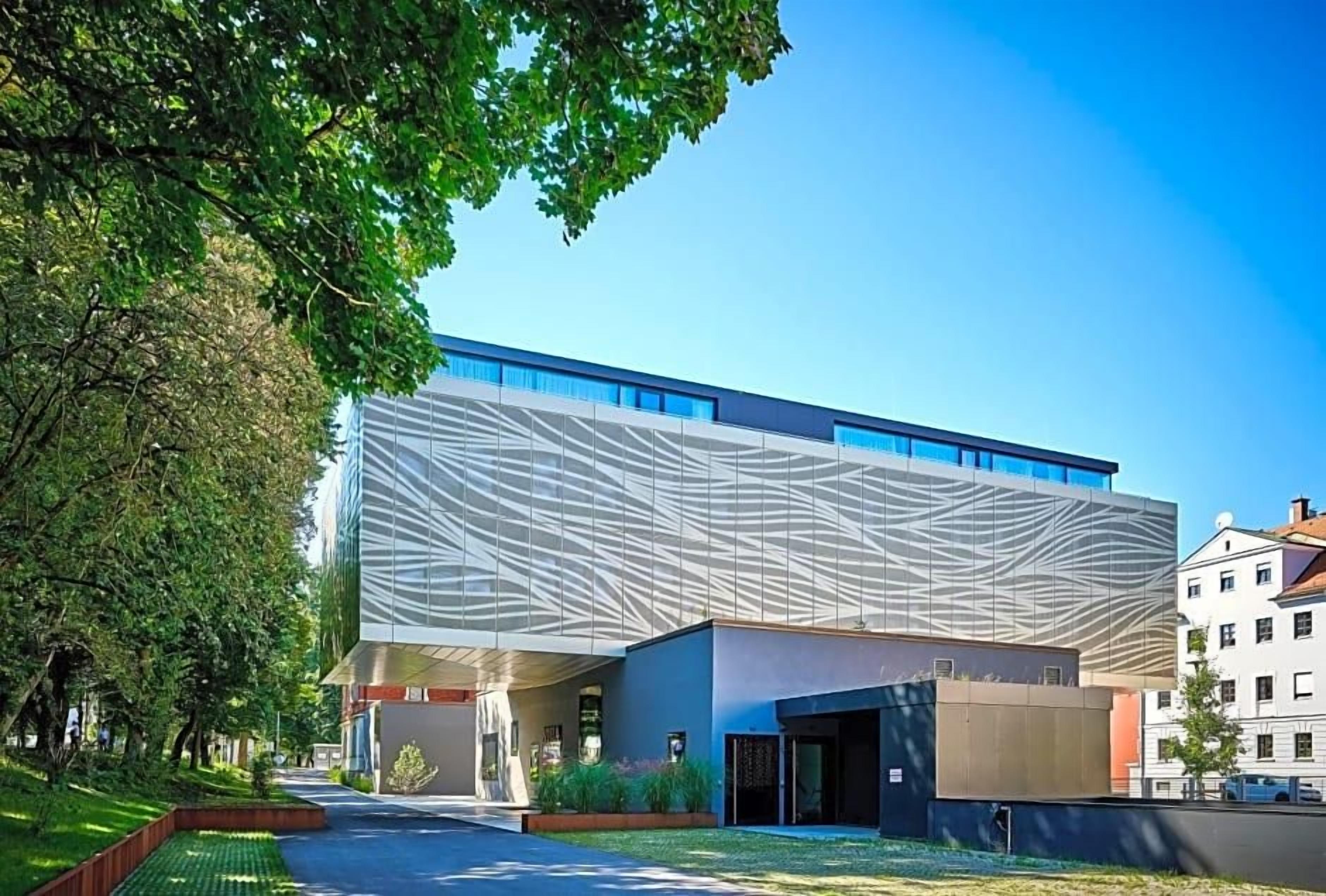 Un edificio moderno con una facciata originale e un ingresso coperto, circondato da un’area ben curata.