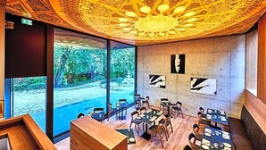 A restaurant with a view of a garden, a patterned ceiling, and artwork on the walls. - Villa Boutique Hotel (Straubing)