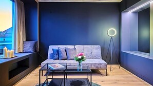 A modern living room with a sofa, a coffee table, a floor lamp, and a window with curtains. - Villa Boutique Hotel (Straubing)