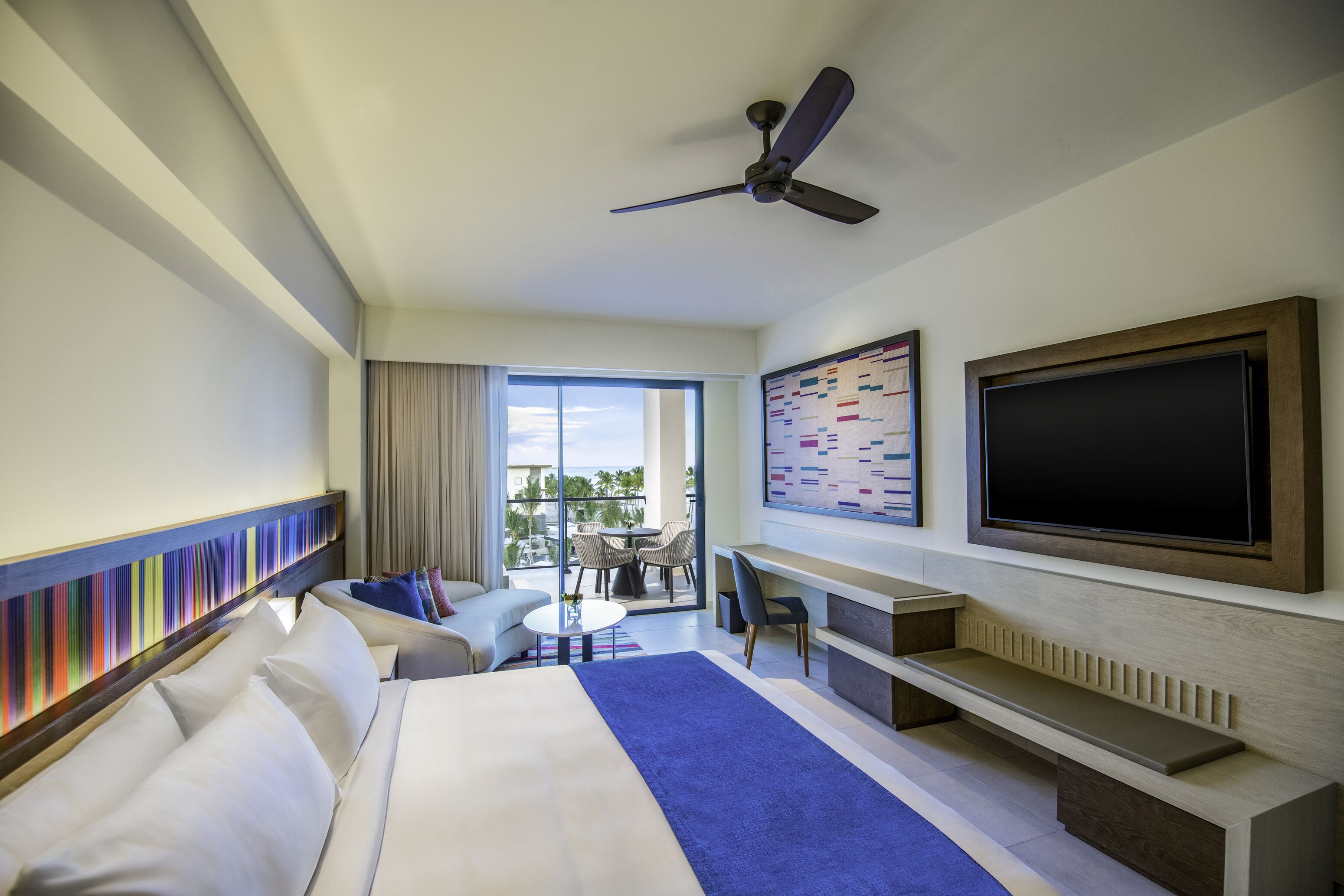 Una habitación de hotel con cama, escritorio, televisor y balcón con vistas.
