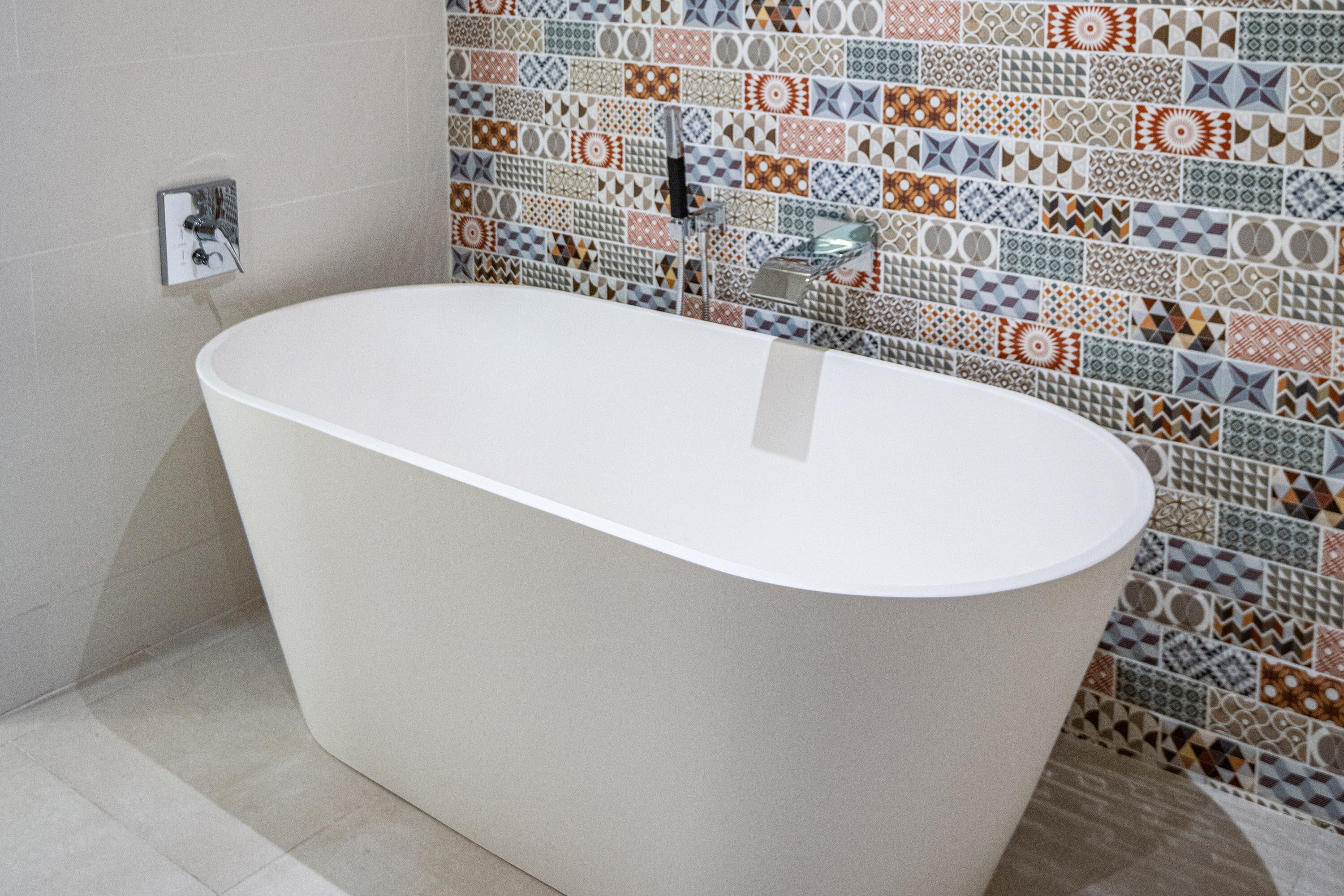 A modern bathroom with a freestanding bathtub, a tiled shower wall, and a visible electrical outlet.