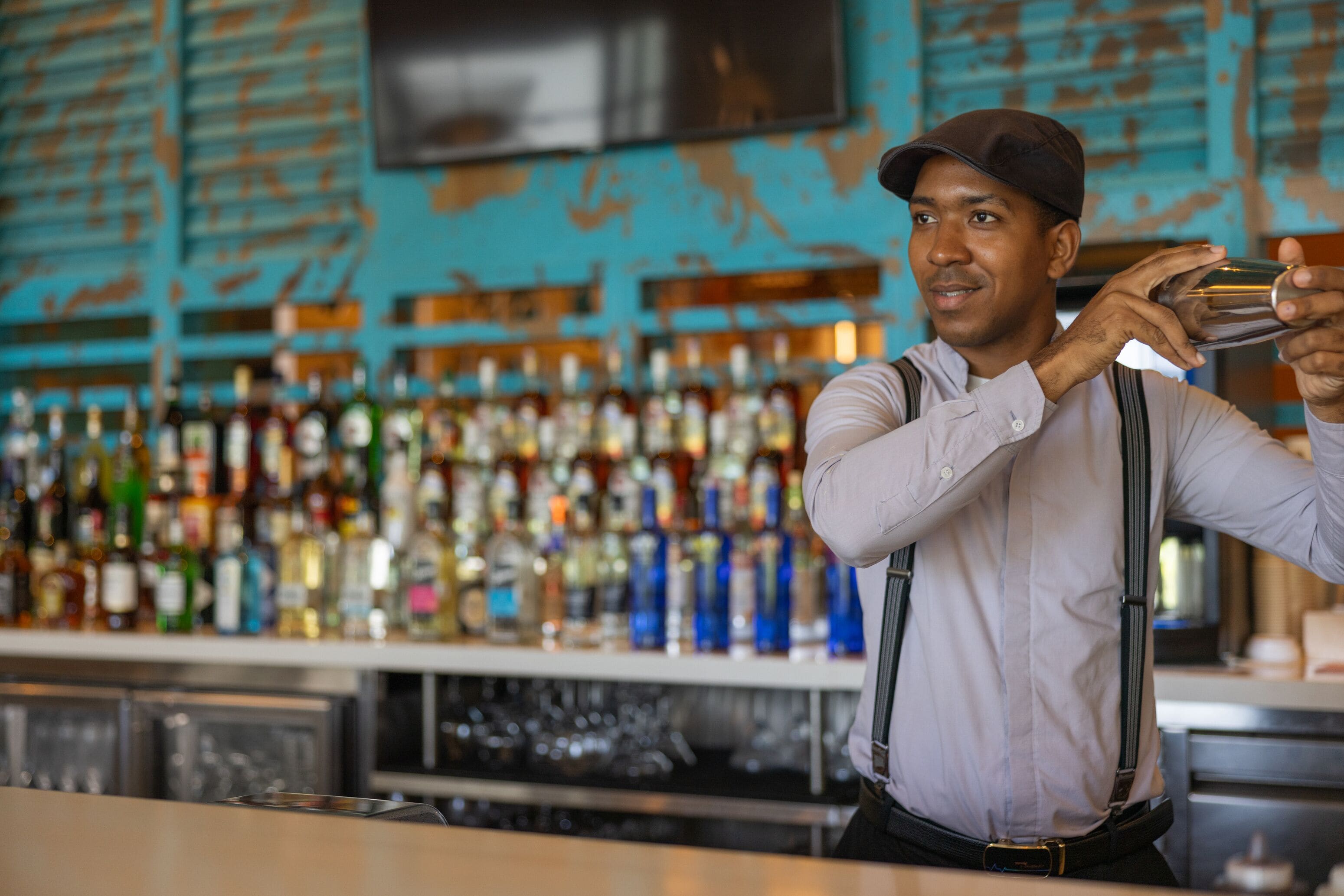 A bartender holding a drink, with a bar stocked with various bottles in the background.