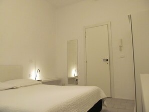 Een slaapkamer met een bed, een nachtkastje, een spiegel en een deur.