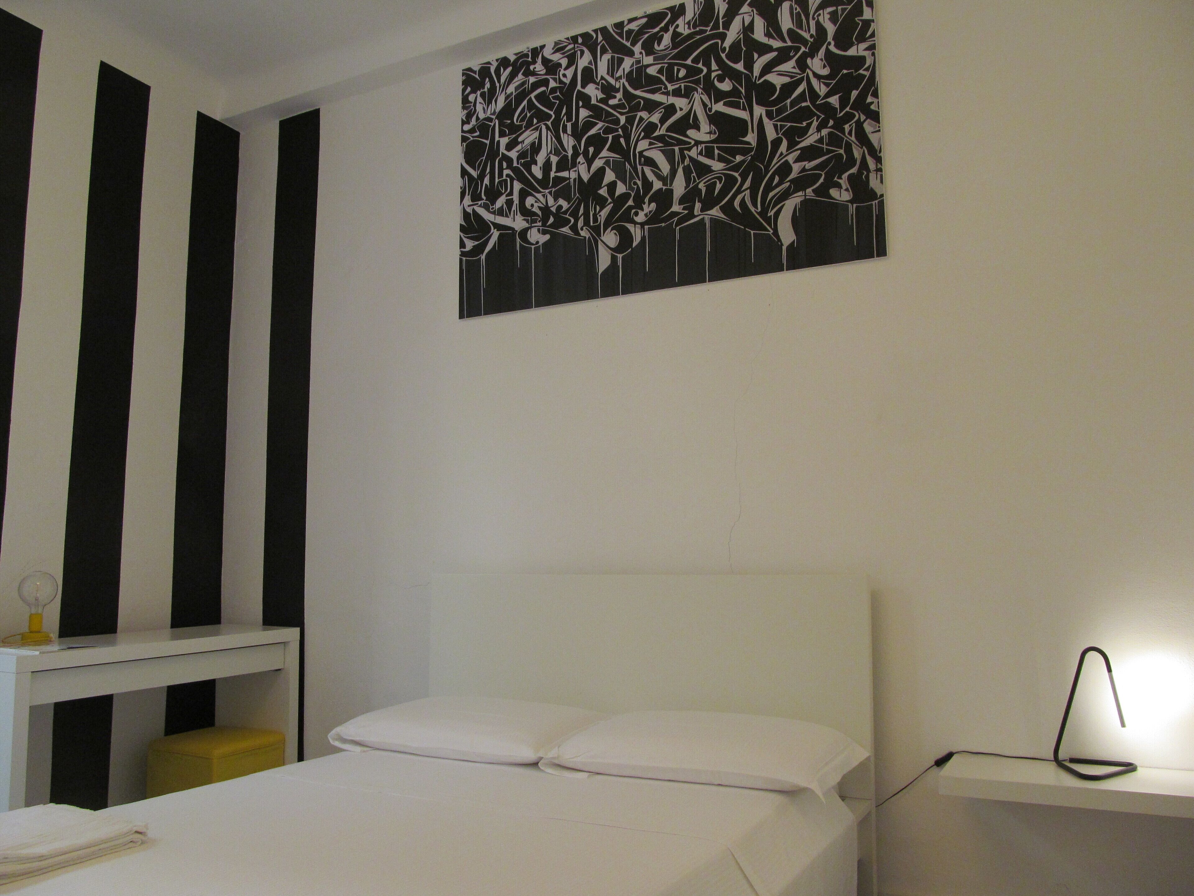 A bedroom with a bed, a bedside table, a nightstand, and a wall art piece.
