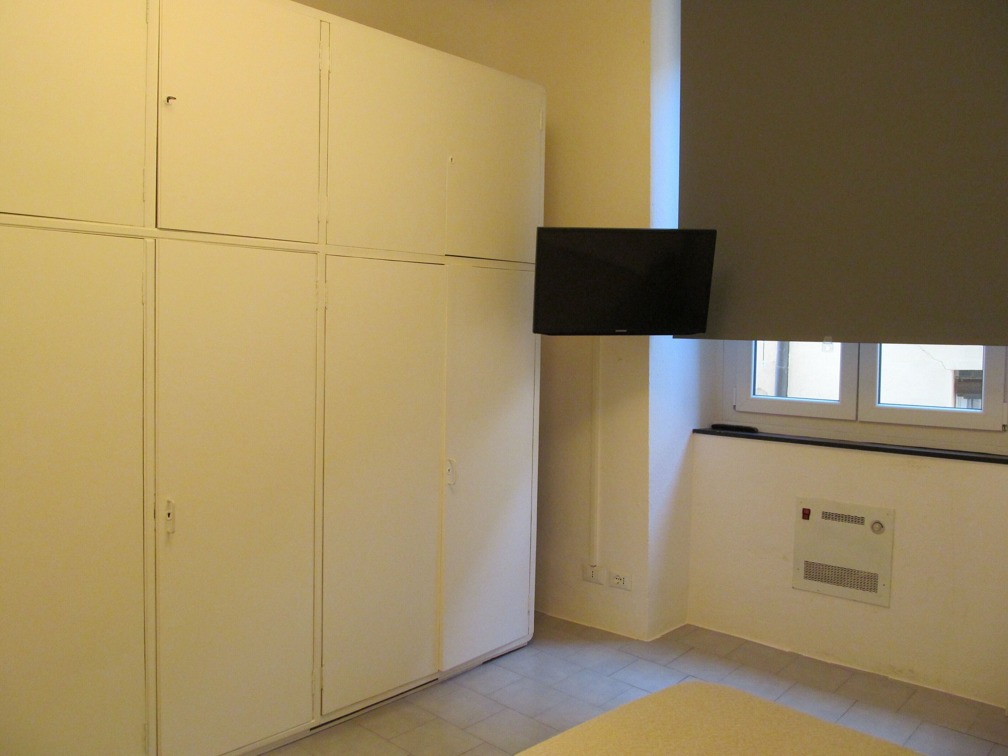 Habitació amb un armari blanc, un televisor de pantalla plana fixat a la paret, una finestra i un aparell d'aire acondicionat encastat a la paret.