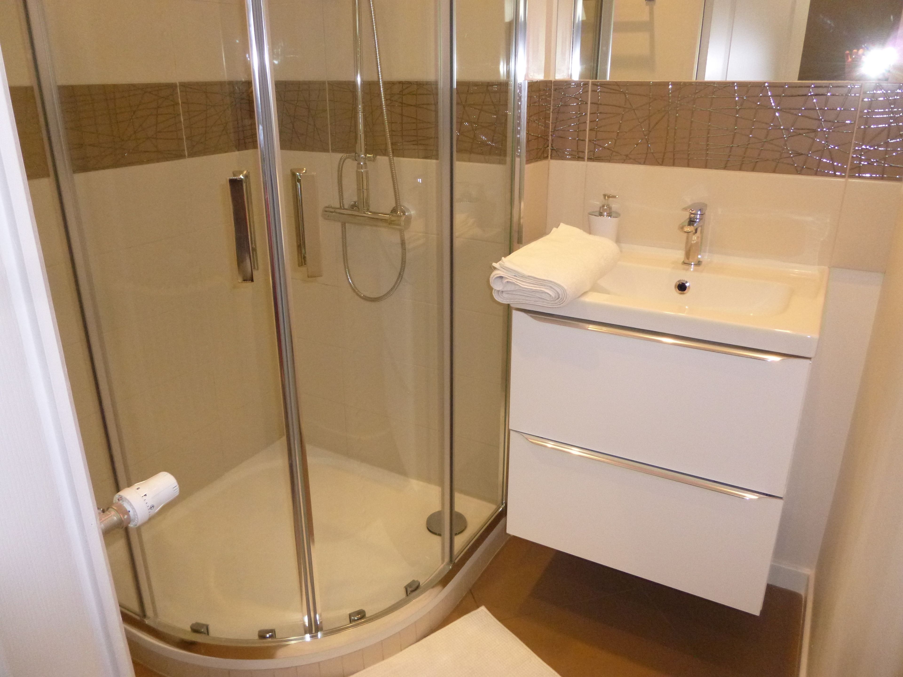 Un baño moderno con ducha de vidrio, lavamanos blanco y espejo sobre él.