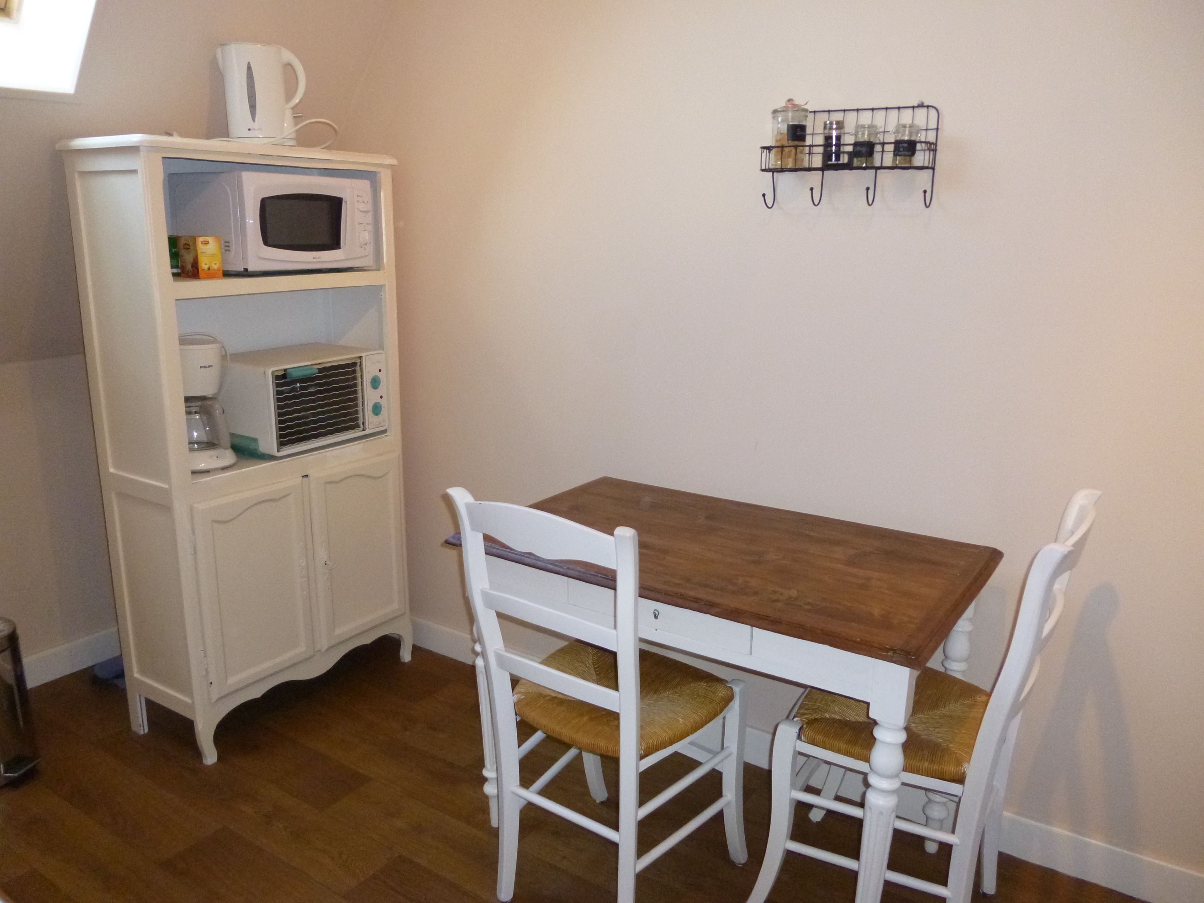 Een compacte keuken met een houten tafel, witte stoelen, een magnetron en een koffiezetapparaat.