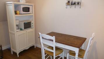 Een compacte keuken met een houten tafel, witte stoelen, een magnetron en een koffiezetapparaat.