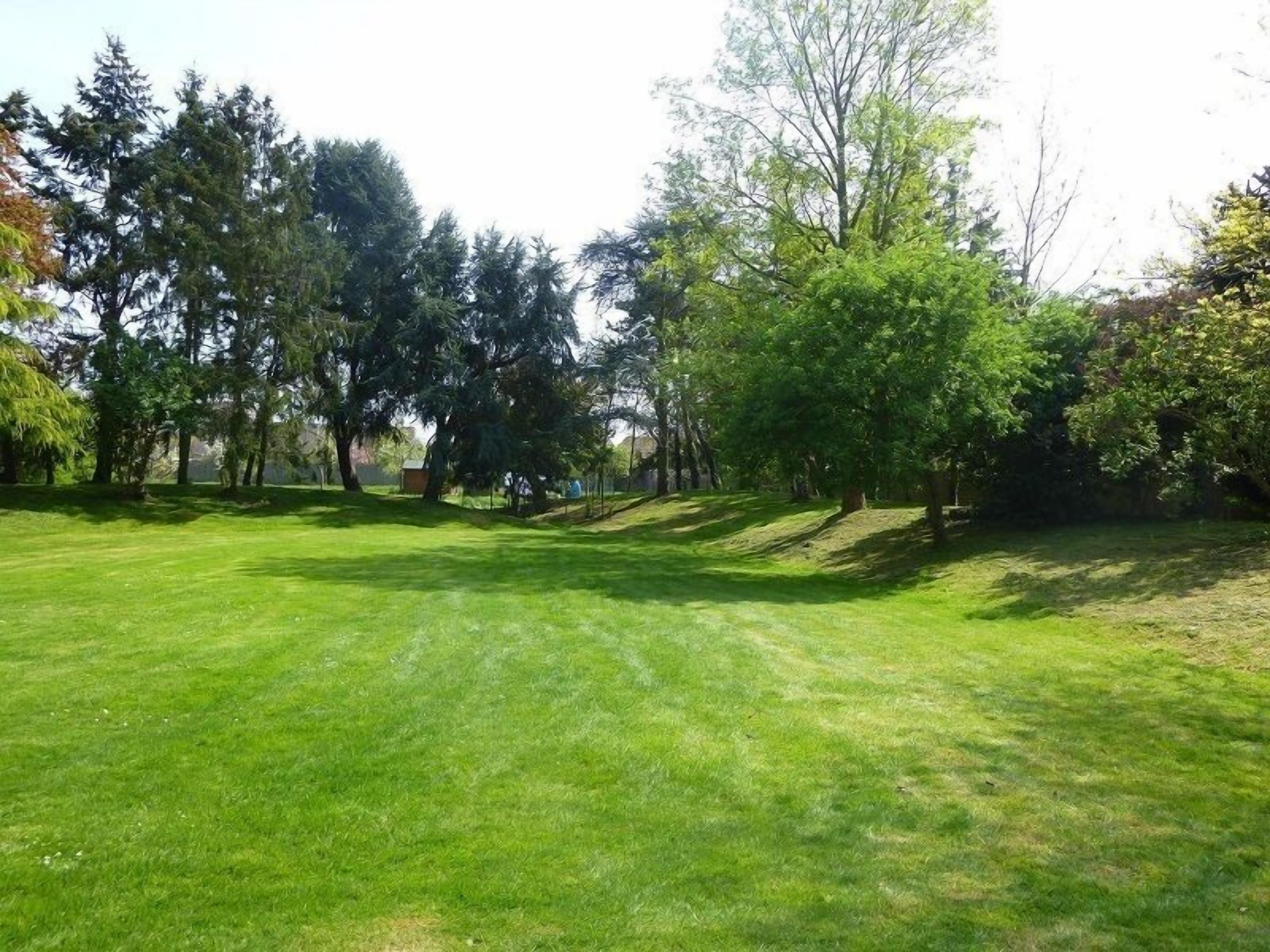 Un área verde bien cuidada con árboles y una pequeña estructura al fondo.