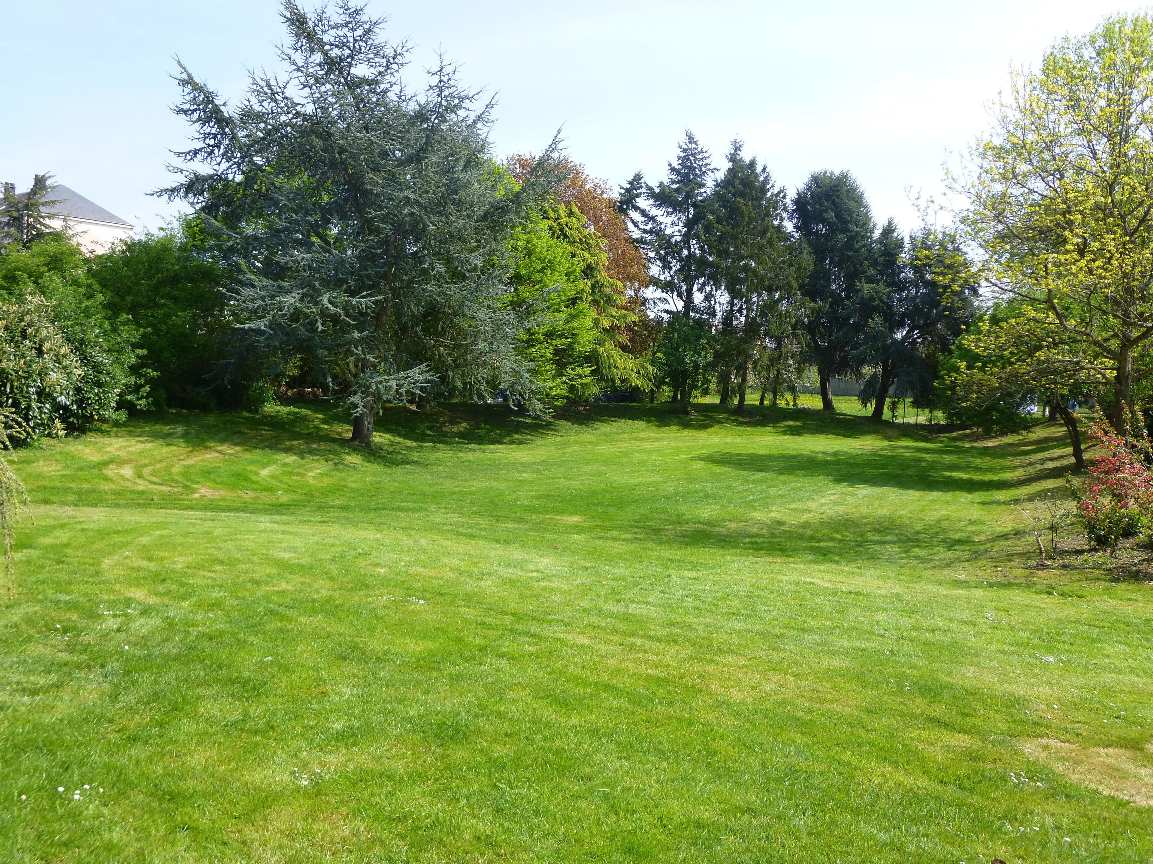 A well-maintained grassy area with trees and a building in the background.