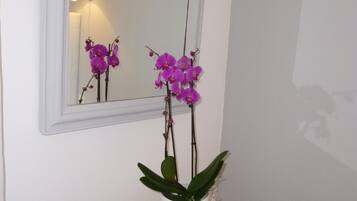 Una orquídea blanca en maceta sobre una mesa blanca con pedestal, frente a una pared blanca con un espejo que refleja la orquídea.