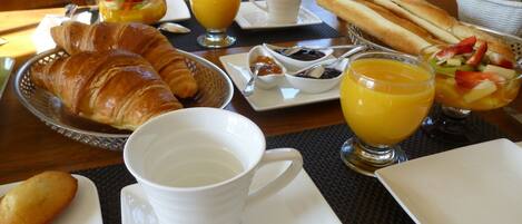 Un desayuno con cruasanes, fruta y jugo de naranja sobre una mesa.