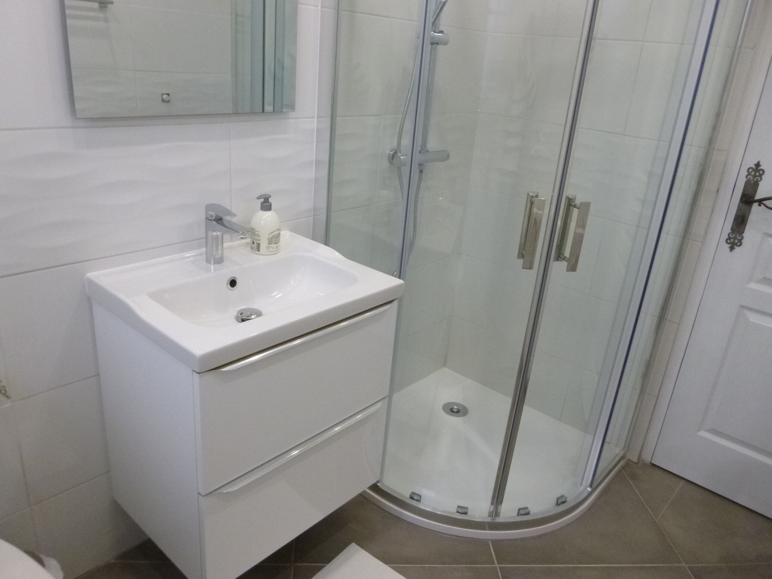 A bathroom with a white sink, a mirror, and a glass-enclosed shower.