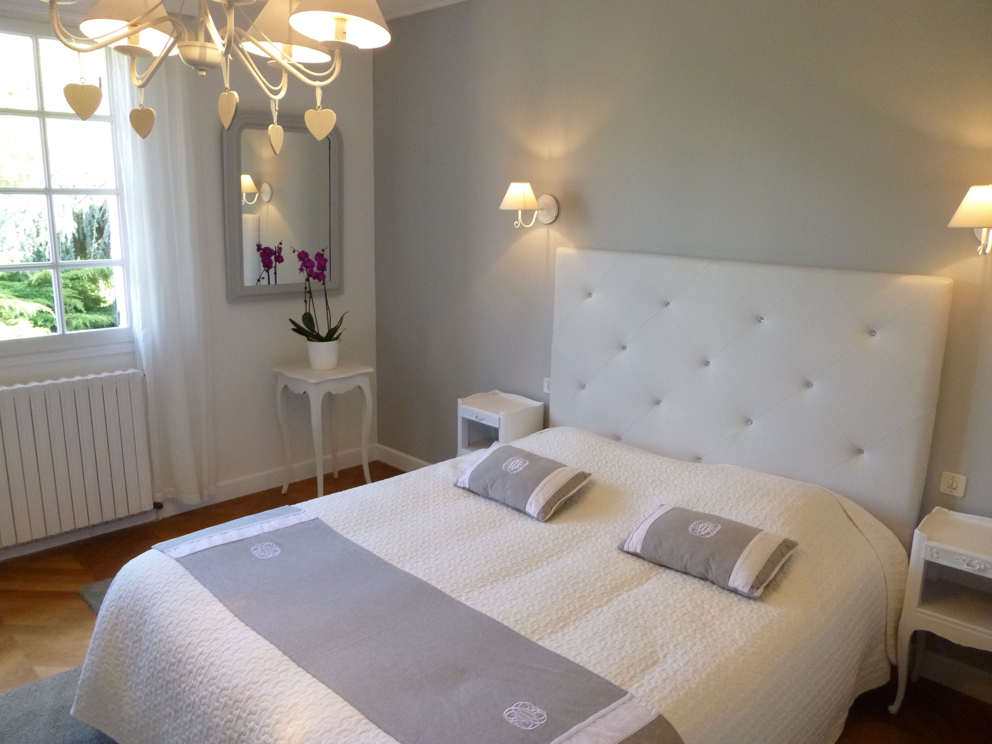 A bedroom with a large bed, white headboard, bedside tables, and a window with curtains.