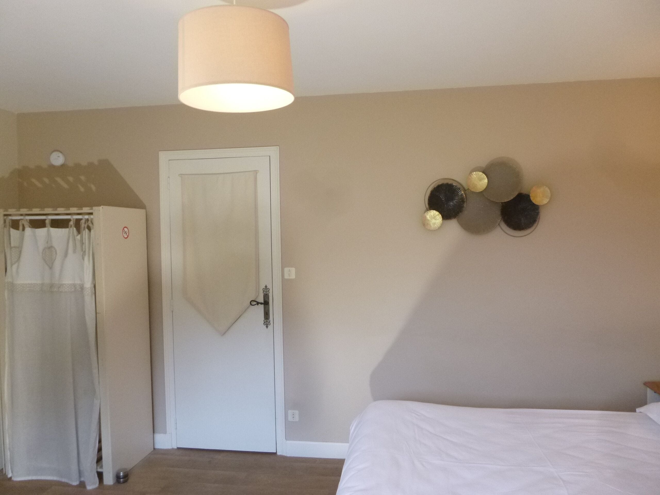 Ein Schlafzimmer mit Bett, Tür, Vorhang, einer Wandleuchte und einer Wanddekoration.