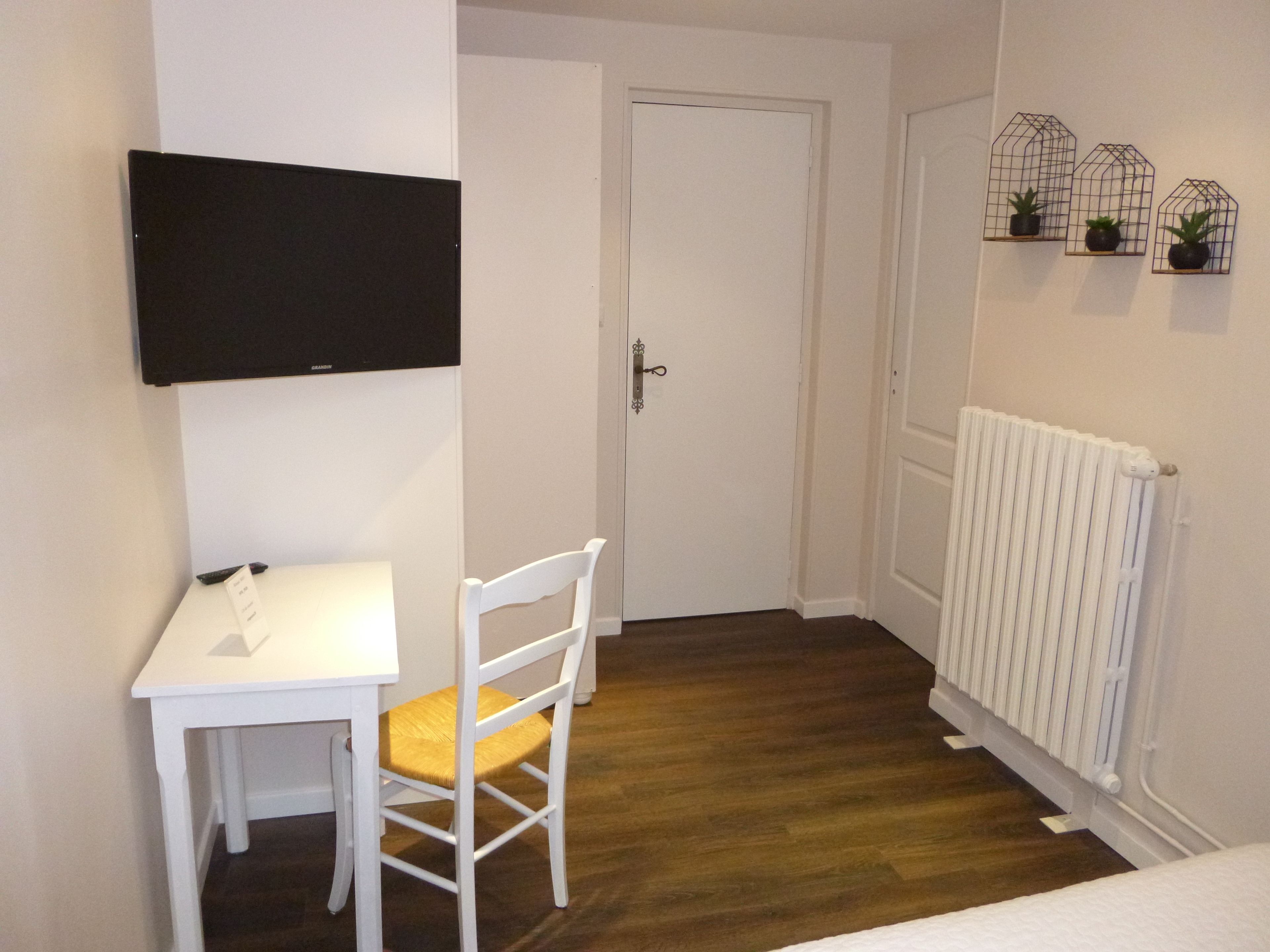 A small room with a white table and chair, a door, a radiator, and three wall-mounted birdcages with plants.