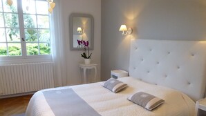 Una cama bien hecha con cabecera blanca, una mesita de noche y otra mesita auxiliar.