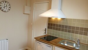 Una cocina compacta con lavavajillas incorporado, un lavamanos y un reloj en la pared.