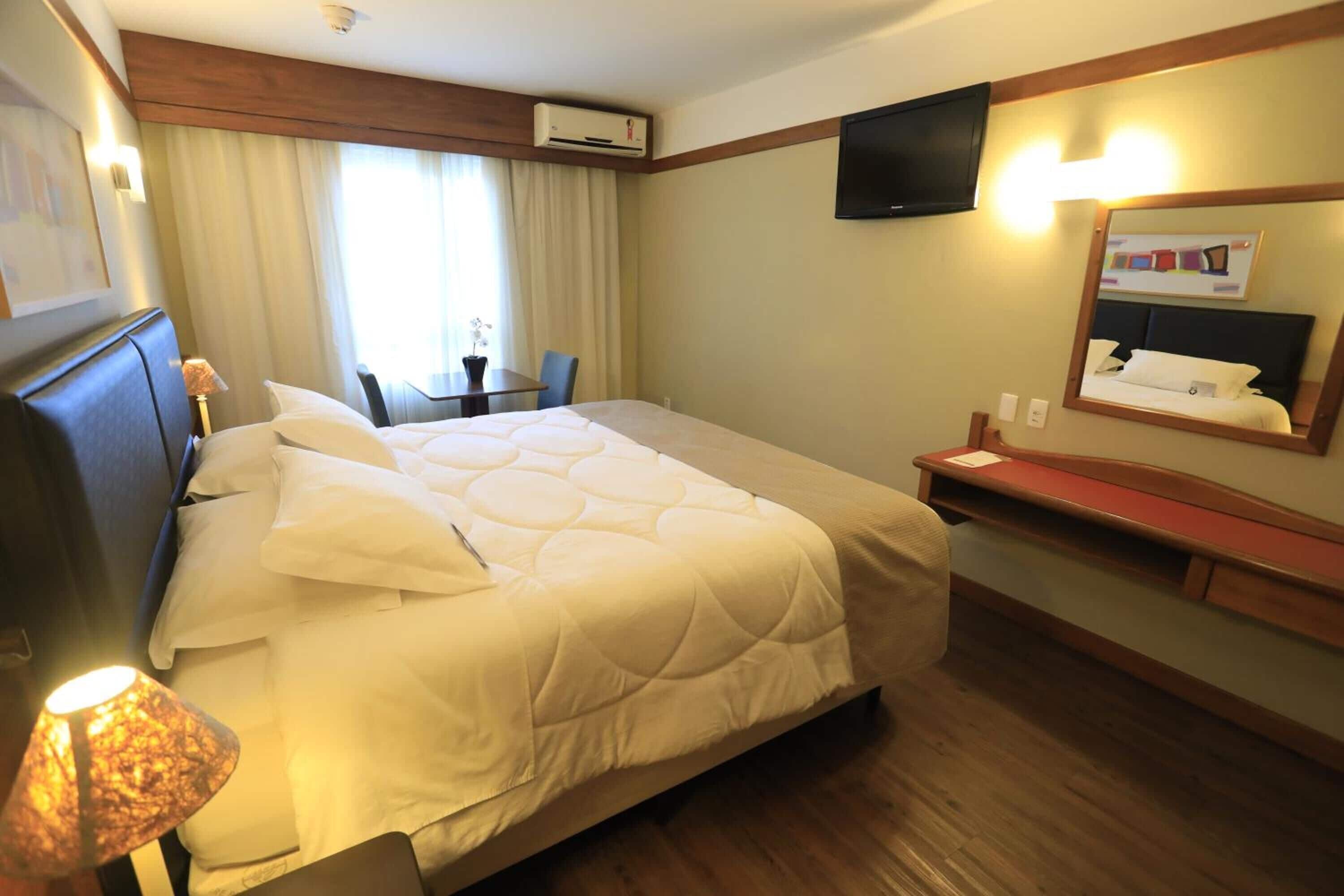 Een hotelkamer met een groot bed, een bureau, een stoel, een televisie en een spiegel.