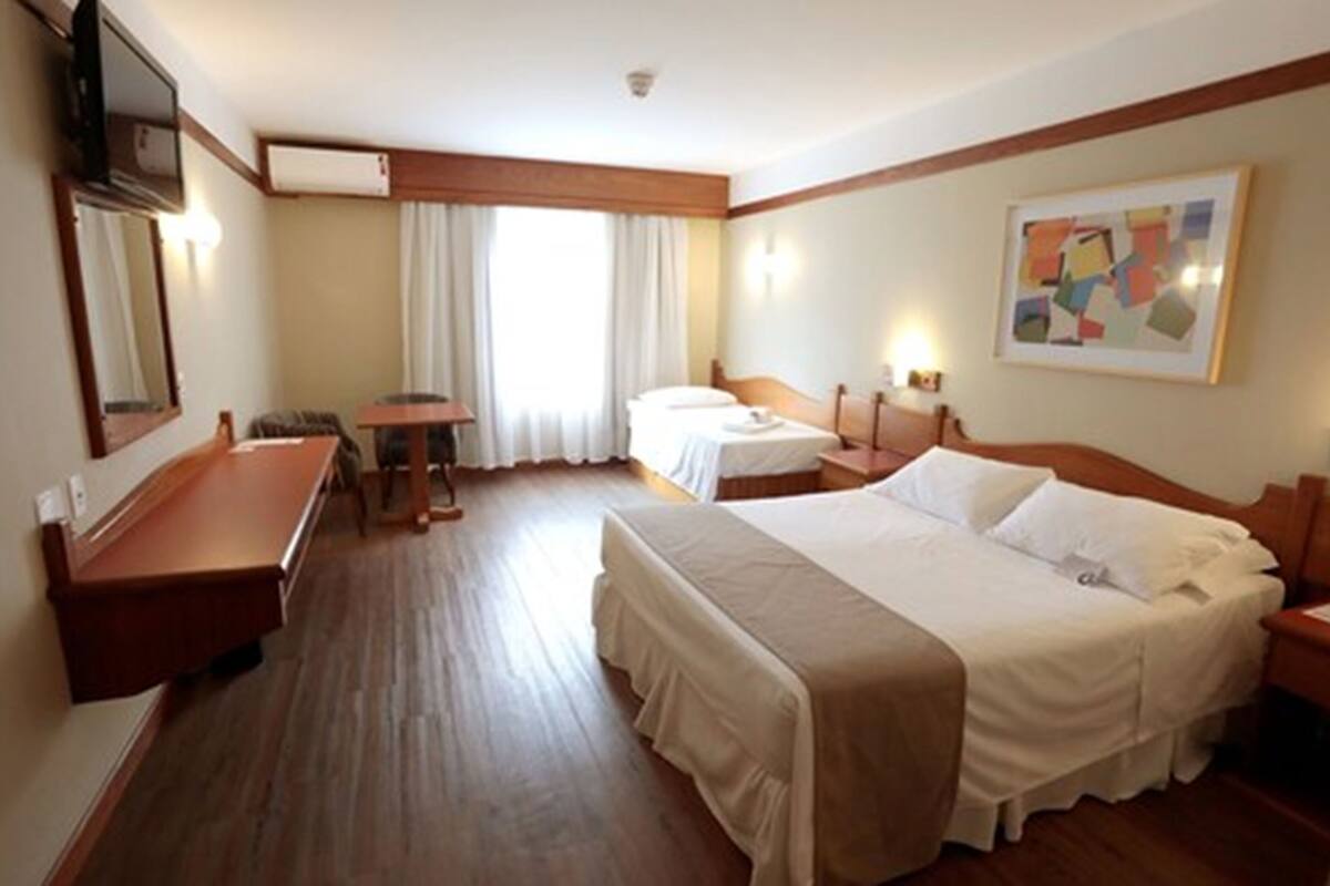 A hotel room with two beds, a desk, a chair, a TV, and a painting on the wall.