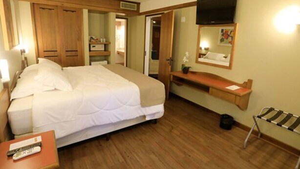 A hotel room with a bed, a TV mounted on the wall, a wooden bench, and a small table with a remote control. - Tri Hotel Canela (Canela)