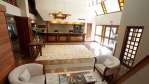 A spacious lobby with a reception desk, two armchairs, a coffee table with magazines, and a large window providing natural light. - Tri Hotel Canela (Canela)