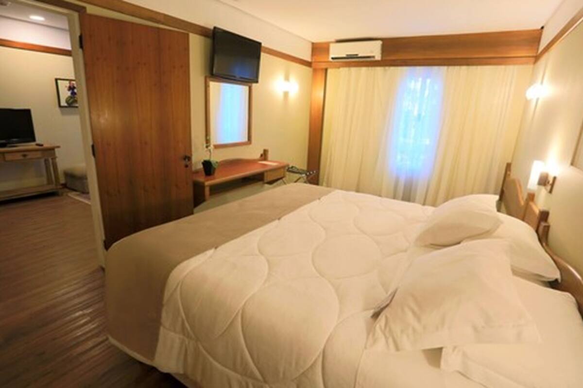 A hotel room with a large bed, a television on a wooden stand, a desk, and a window with curtains.