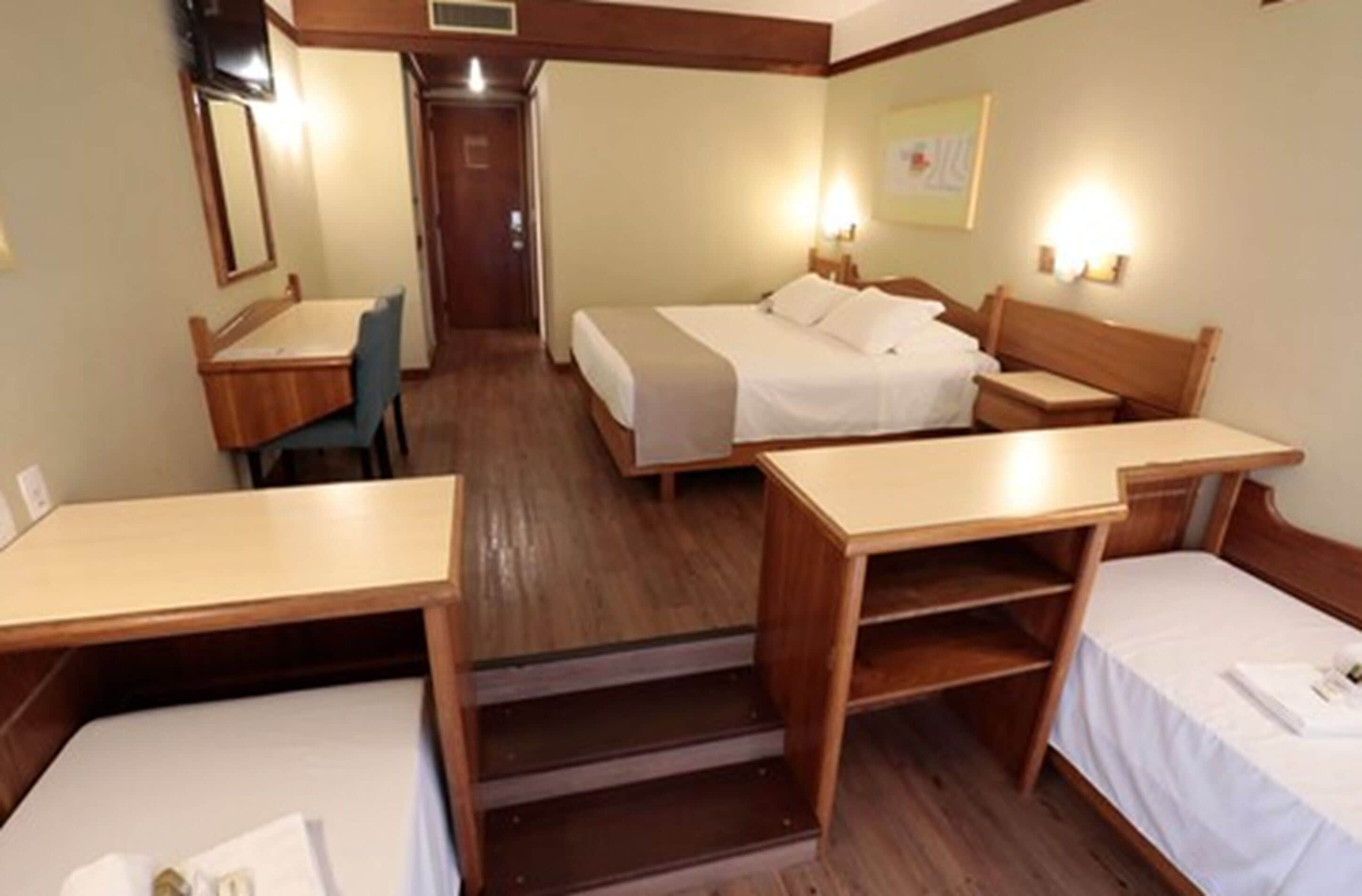 A hotel room with two single beds, a wooden desk, a chair, and a small table.