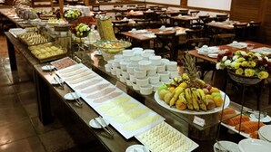 A buffet with various food items and beverages, arranged on a long table in a dining area with multiple tables and chairs. - Tri Hotel Canela (Canela)
