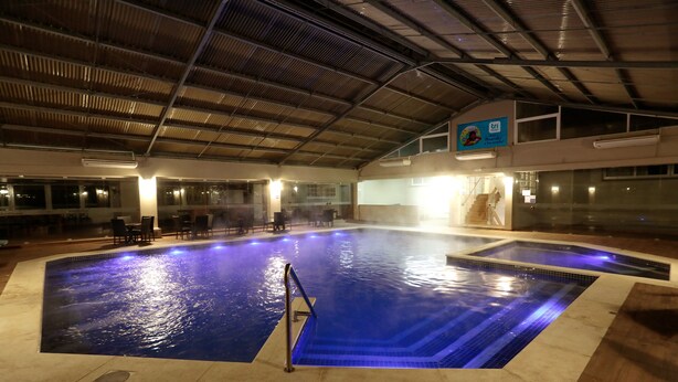 An indoor swimming pool with a tiled edge, a metal ladder, and a covered area with a roof. - Tri Hotel Canela (Canela)