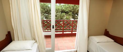 A room with two single beds, a wooden ceiling, a sliding glass door to an outdoor area with a red railing, and an air conditioning unit on the wall.