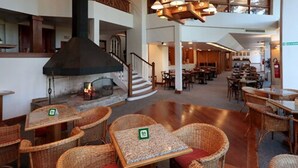 A spacious lobby with wicker furniture, a fireplace, and a staircase leading to an upper level. - Tri Hotel Canela (Canela)