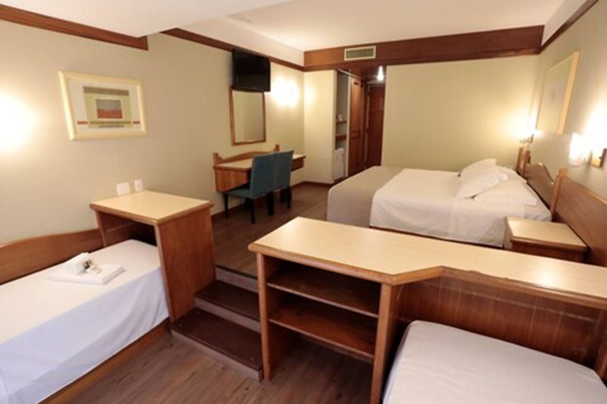 A hotel room with two single beds, a desk, a chair, and a small table.