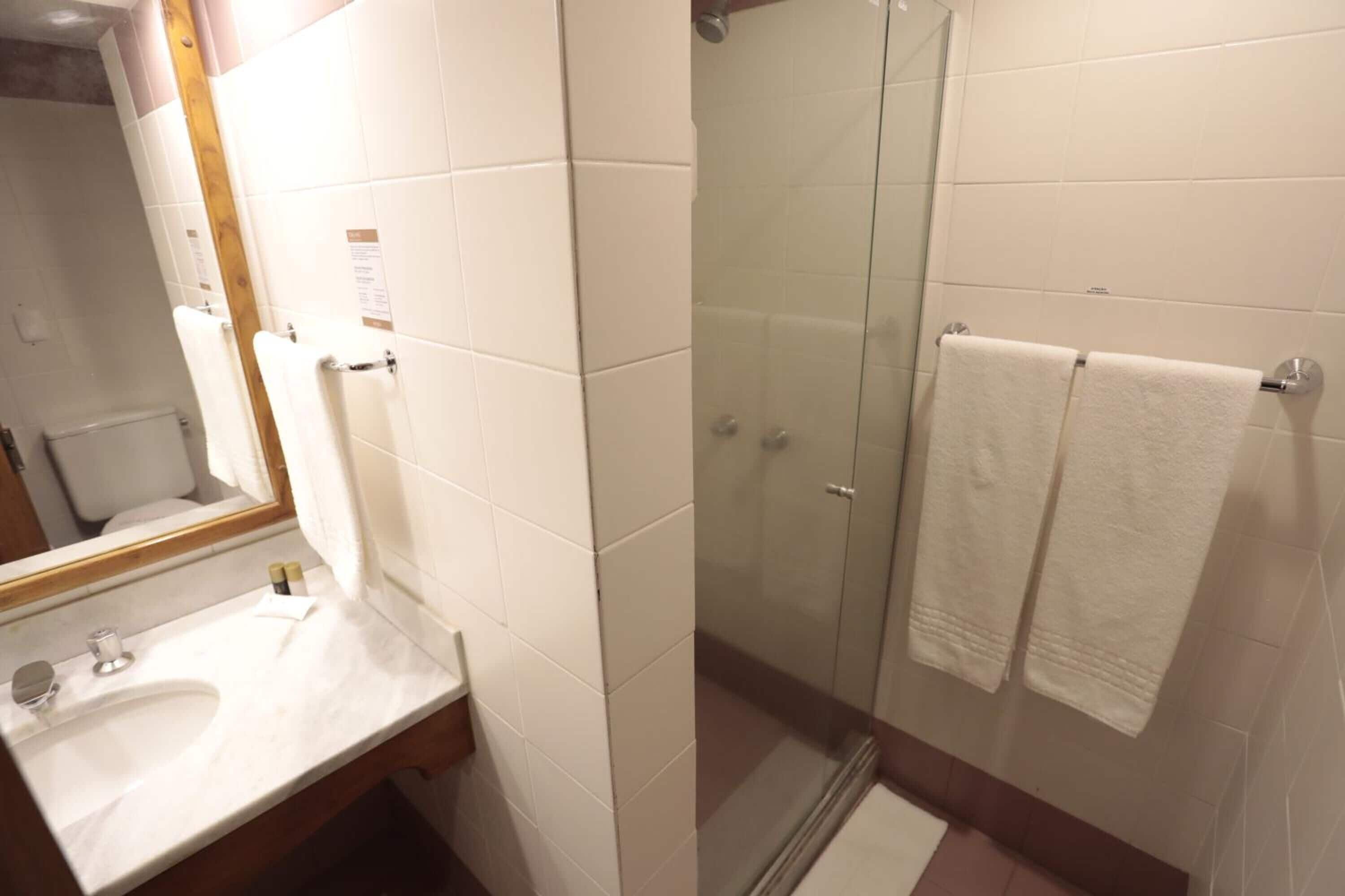 Un baño con lavamanos blanco, espejo y ducha con mampara de vidrio.