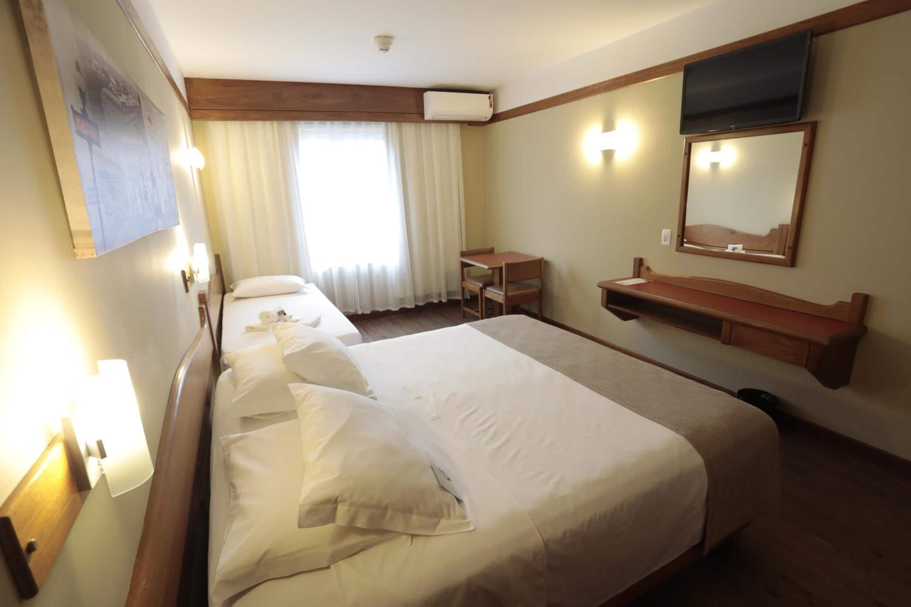 Una habitación de hotel con una cama grande, un escritorio, una silla, un televisor y un espejo.