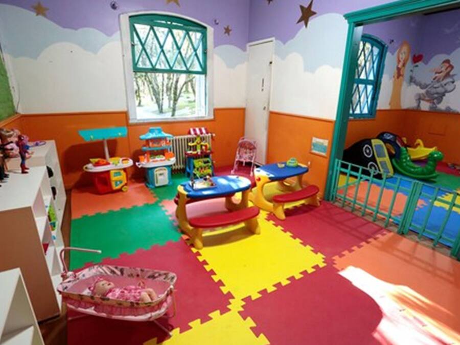 Uma sala de recreação infantil com tapetes de jogos coloridos, brinquedos e uma mesa de brincar.