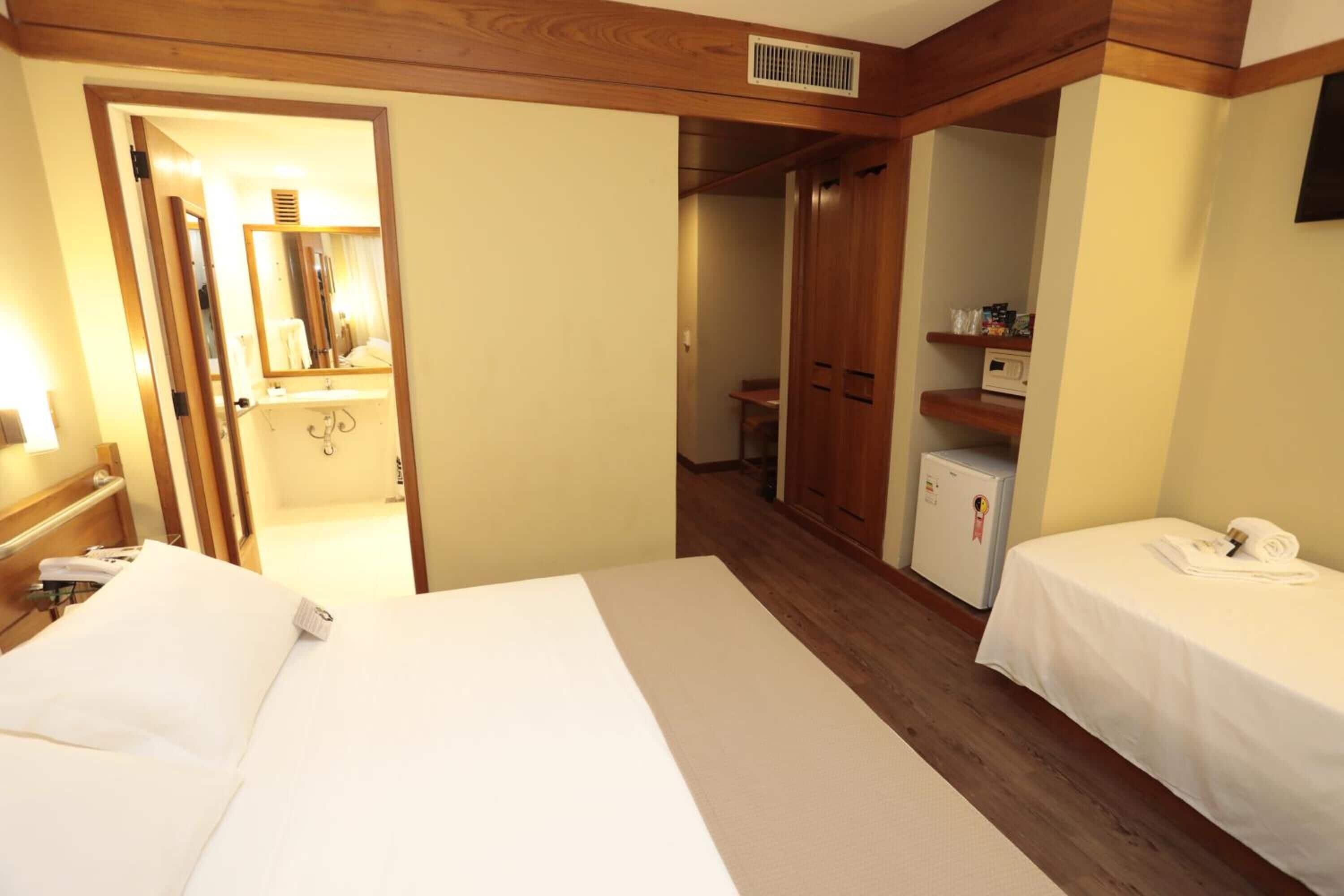 A hotel room with a large bed, a smaller bed, a wardrobe, a mirror, and a small refrigerator.